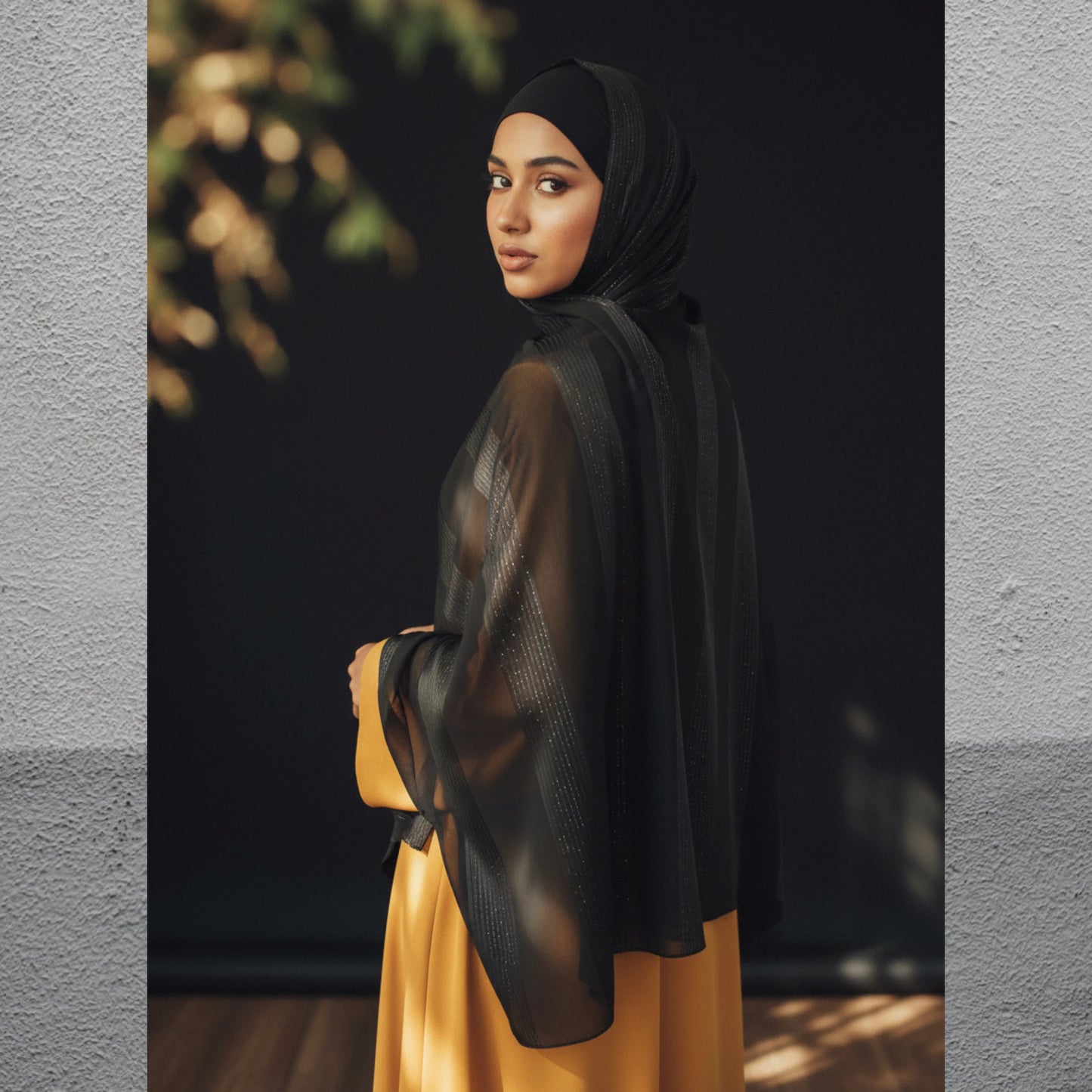Woman wearing a black hijab and yellow dress against a dark background