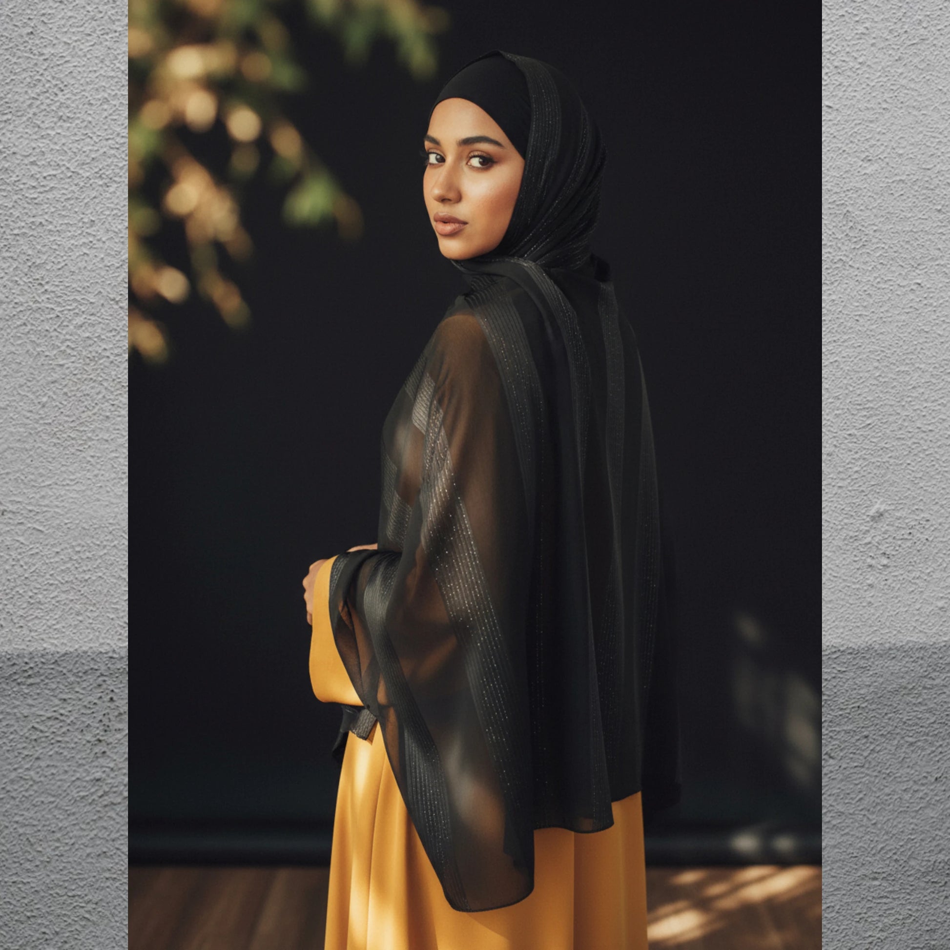 Woman wearing a black hijab and yellow dress against a dark background